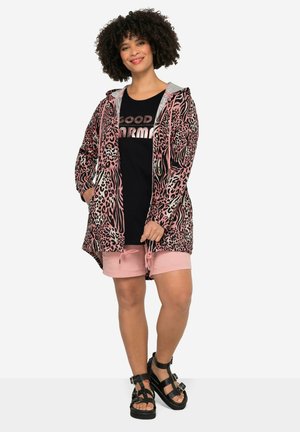 Cardigan en imprimé léopard rose et noir avec capuche, associé à un t-shirt noir et un short à cordon rose. Sandales noires à lanières.