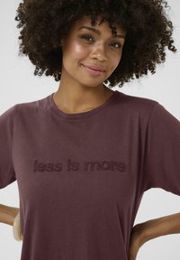 Bordeaux katoenen t-shirt met de verhoogde tekst "less is more" in een bijpassende kleur, met een klassieke ronde halslijn en korte mouwen.