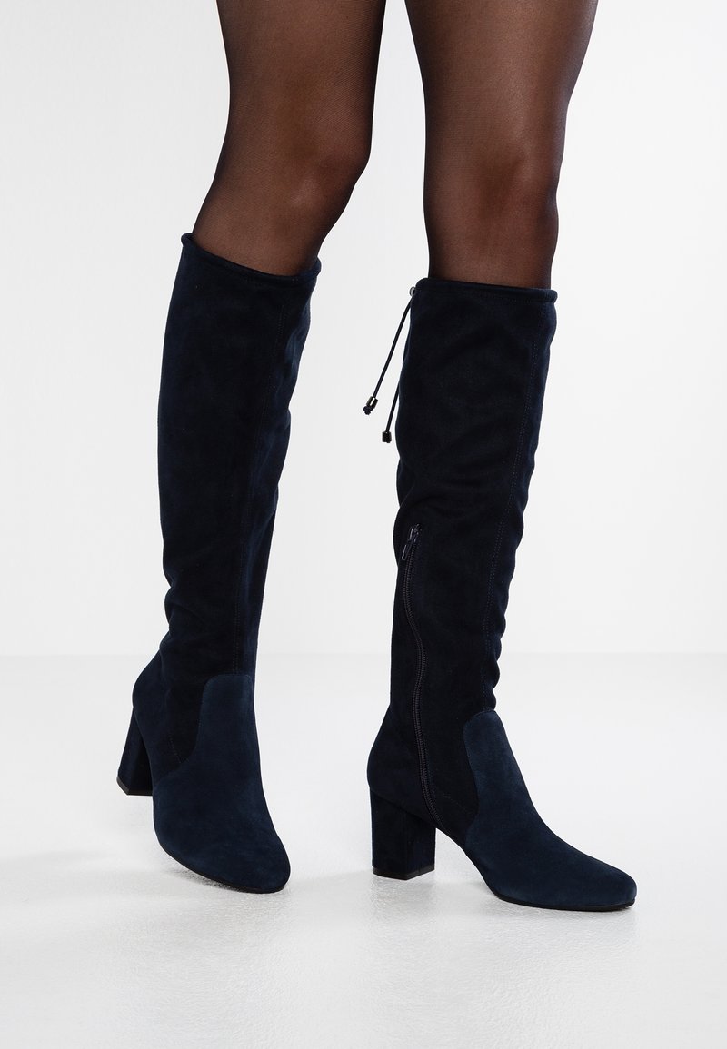 Knähöga stövlar i marinblå mocka med klackar, med texturerade paneler och inre dragkedjor för enkel användning.