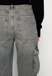 Pantalones cargo de mezclilla azul claro con un corte relajado, que cuentan con dos bolsillos traseros y un bolsillo lateral de utilidad. Costuras cosidas y tela texturizada.