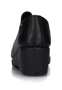 Scarpa zeppa in pelle nera vista da dietro con cuciture visibili e suola spessa su sfondo bianco.