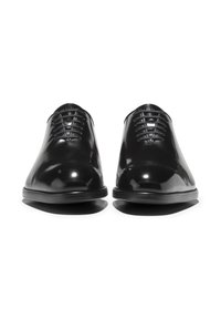 Pár lesklých černých kožených formálních společenských bot s tkaničkami, zobrazených zepředu na bílém pozadí.