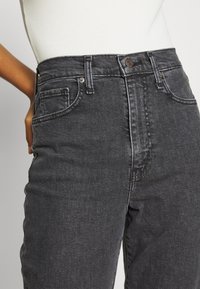 Jeans en denim gris foncé taille haute avec un design classique à cinq poches, des coutures contrastantes et une fermeture à bouton à la taille.