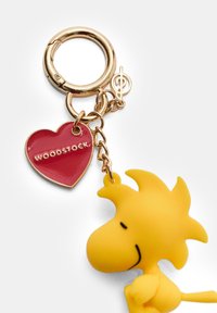 Keltaiset kumiset Woodstock-hahmoavaimenperä, joka on kiinnitetty kullanväriseen metallirenkaaseen. Avaimenperässä on punainen sydänmerkki, johon on kaiverrettu teksti "WOODSTOCK."