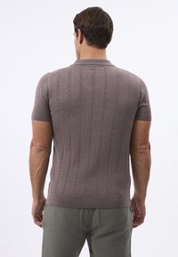 Korte mouwen gebreide polo in gedempt mauve, met een gemêleerd patroon en geribde kraag en zoom, gecombineerd met licht olijfgroene broeken.