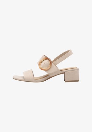 Beige Wildledersandale mit kleinem Blockabsatz, offenen Zehen und breiten Riemen, die mit einem kreisförmigen goldenen Akzent verziert sind.