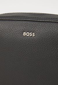Borsa in pelle nera texture con un prominente logo dorato "BOSS". La superficie ha una finitura in rilievo con dettagli di cucitura discreti.