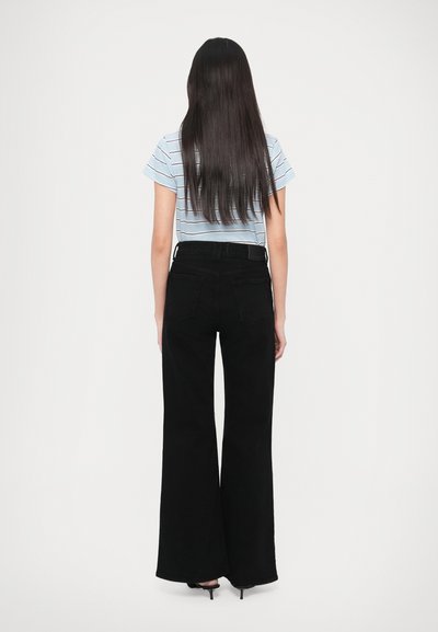 Musta leveälahkeiset farkut yhdistettyinä siniraidalliseen t-paitaan, jossa on lyhyet hihat ja vartalonmyötäinen malli, nähtynä takaa.