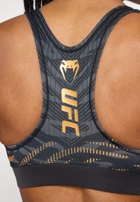 Sujetador deportivo negro con toques dorados, que presenta un patrón de piel de serpiente, diseño elegante y costuras reforzadas para mayor soporte.