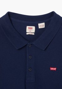 Marinblå polo t-shirt i bomull med krage, tre knappar och en liten röd Levi's-logotyp på vänster bröst.