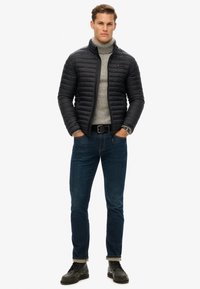 Chaqueta de plumas negra, suéter de cuello alto gris, jeans azules, cinturón negro, reloj plateado y zapatos negros. Líneas limpias, textura acolchada en la chaqueta.