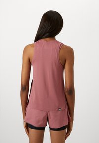 Raspberry-colored athletic tank top with a loose fit, side slits, and a tag at the bottom. Paired with matching shorts.