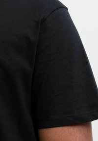 Sort kortærmet t-shirt lavet af bomuld, med en glat tekstur og en simpel rund halsudskæring, med synlige sømdetaljer.