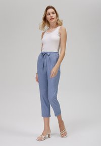 Light blue, textured, cropped trousers with a tied waistband. Paired with a fitted white tank top and strappy sandals.