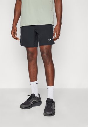 Schwarze Nike-Shorts aus feuchtigkeitsableitendem Material, kombiniert mit weißen Sportsocken und schwarzen Sportschuhen mit einem strukturierten Design.