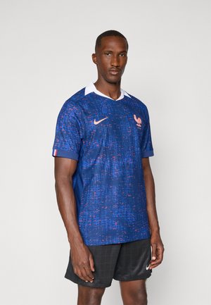Maglia da calcio blu con motivo texture, colletto bianco e logo arancione. Presenta un emblema sul petto e colori di accento sulle maniche.