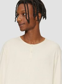 Helles beige Langarmhemd mit rundem Ausschnitt und dreiknopfigem Verschluss. Baumwollmaterial mit glatter Textur und lässiger Passform.