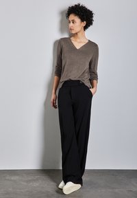 Pullover marrone a scollo a V, maniche lunghe, abbinato a pantaloni neri larghi con bottone in vita. Sneakers bianche con suole testurizzate.