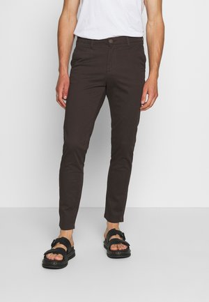 Bruna, smala byxor av bomull med en slät textur, utrustade med en enda knappstängning, bärs med svarta sandaler.