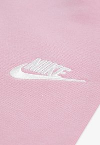 Rozā Nike apģērbs ar teksturētu audumu un izšūtu balto logo. Dizains ir vienkāršs, koncentrējoties uz logo izteiksmīgo formu.