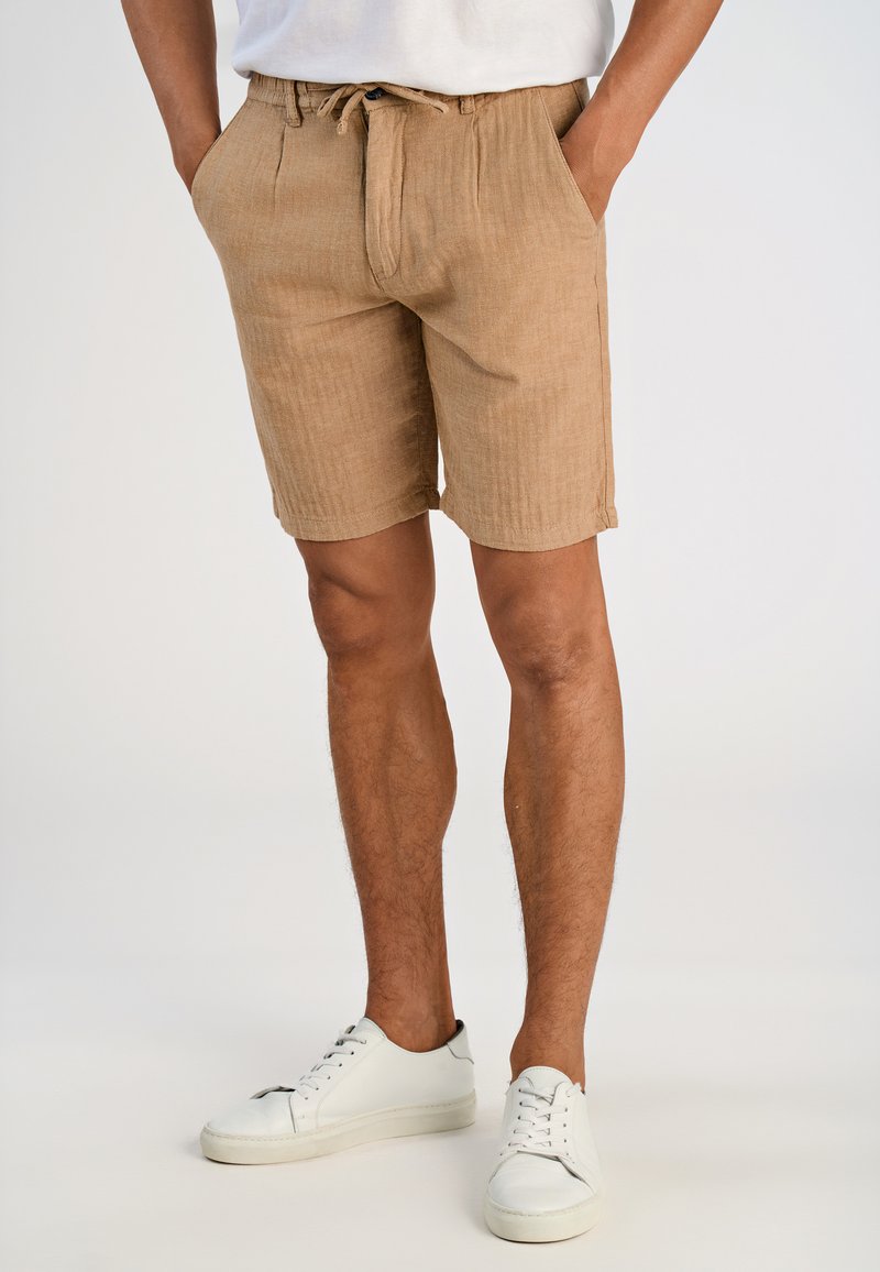 Beiga linnen shorts med en strukturerad tyg, elastisk midja och sidofickor. Matchas med vita lågt skurna sneakers.