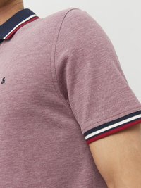 Burgunderfarvet polo t-shirt med tekstureret stof, der har en marineblå krave og stribede røde, hvide og blå detaljer på ærmerne.