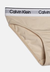 Beige Calvin Klein alsónemű, puha, sima textúrával, kontrasztos fehér derékkal, fekete betűzéssel.