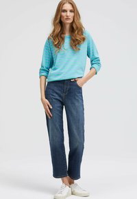 Helles blau gestreiftes Langarmoberteil kombiniert mit dunkelblauen Jeans. Die Jeans haben einen geraden Schnitt, und das Model trägt weiße Sneaker.