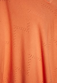 Lyse orange strikket stof med en blød tekstur, der har stjerneformede perforeringer og en V-hals design.