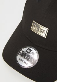 Fekete, állítható sapka, amely szövetből készült, arany színű fém logótáblával és "9FORTY ADJUSTABLE" feliratú kör címkével. Texturált felület.