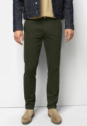 Chinos vert foncé en tissu sergé, avec une coupe ajustée et des poches avant discrètes. Associés à des bottes en suède marron clair.
