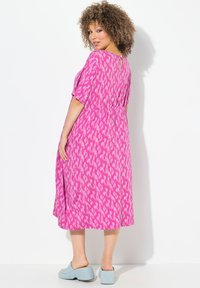 Abito rosa con un design a fantasia, maniche corte, cucitura in vita e un dettaglio a chiave sulla schiena. Abbinato a mule platform azzurri.
