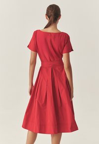 Piros pamut ruha négyzet alakú nyakkivágással, rövid ujjakkal és megkötött derékrésszel. Redők találhatók a deréktól a bővülő szoknyáig.