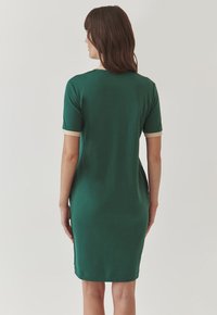 Green fitted dress with short sleeves, cream trim on sleeves and neckline, smooth fabric, knee-length design, no visible patterns or embellishments.