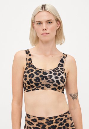 Woman with short blonde hair wearing leopard print crop top and matching bottoms, showing butterfly tattoo on left upper arm.