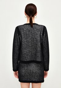 Svart och vit stickad klänning i en texturerad tyg, med långa ärmar och en figurnära siluett. Avslutad med en kontrasterande svart kant.