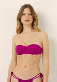 Top bikini bandeau push-up magenta con dettagli arricciati. Abbinato a slip bikini minimali con lacci regolabili. Texture liscia.