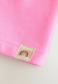 Tissu rose avec une texture lisse, comportant une étiquette avec un motif de arc-en-ciel dans des tons de marron sur un fond beige.