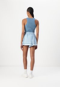 Modrá žebrovaná tílko spárovaná s modrými vzorovanými šortkami s elastickým pasem a bílým lemováním. Modelka nosí bílé tenisky a ponožky do poloviny lýtek.