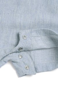 Coin d'une chemise en lin bleu clair avec des boutons-pression argentés. Le tissu présente une texture tissée, mettant en valeur les détails fins et les coutures.