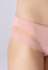 Gros plan d'une personne portant des sous-vêtements rose clair sans coutures avec un détail en maille sur la zone latérale des hanches.
