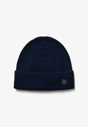 Donkerblauwe geribbelde gebreide muts met omgeslagen boord en een klein vierkant zwart-wit logoplaatje aan de voorkant van de boord.