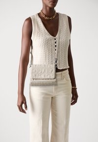 Bežový pletený sveter s výstrihom do V, v kombinácii so svetlo béžovými džínsami. Krémová crossbody taška s embosovaným textom a striebornými doplnkami.