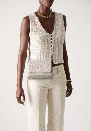 Felpa lavorata a maglia beige con scollo a V, abbinata a jeans beige chiaro. Borsa a tracolla color crema con testo in rilievo e accessori in argento.