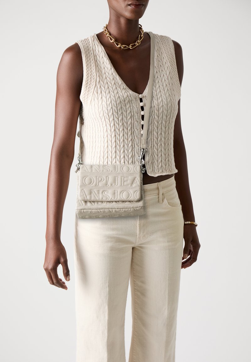 Bežový pletený sveter s výstrihom do V, v kombinácii so svetlo béžovými džínsami. Krémová crossbody taška s embosovaným textom a striebornými doplnkami.