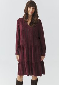 Robe longue bordeaux à manches longues avec décolleté en V, présentant de subtils motifs géométriques, une jupe à volants et des poignets à bouton, fabriquée en tissu léger.