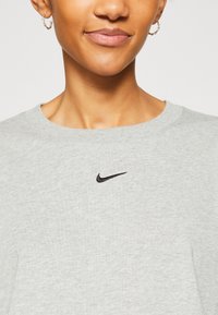 Sudadera de algodón gris con cuello redondo y pequeño logo negro de Nike en el pecho. Textura suave y ajuste relajado.