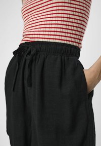 Sorte linnedbukser med elastisk talje og bindebånd. Har sidelommer og en afslappet pasform, der fremhæver en blød tekstur.