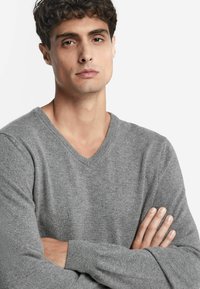 Grauer V-Ausschnitt-Pullover aus weichem, texturiertem Stoff. Verfügt über lange Ärmel und eine lockere Passform. Auffällige Nahtdetails am Ausschnitt.