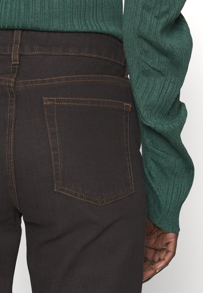 Καφέ τζιν παντελόνι με αντίθετη κίτρινη ραφή, που διαθέτει πίσω τσέπη και φοριέται με textured πράσινο ριμπ πουλόβερ.